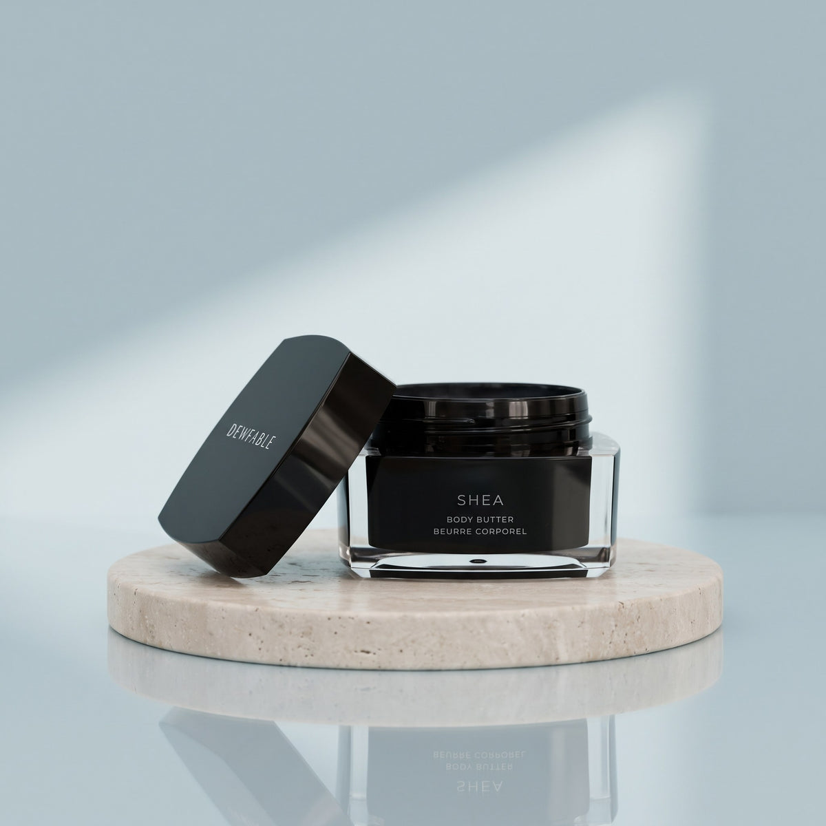 Shea Body Butter jar and lid on a pale stone plinth