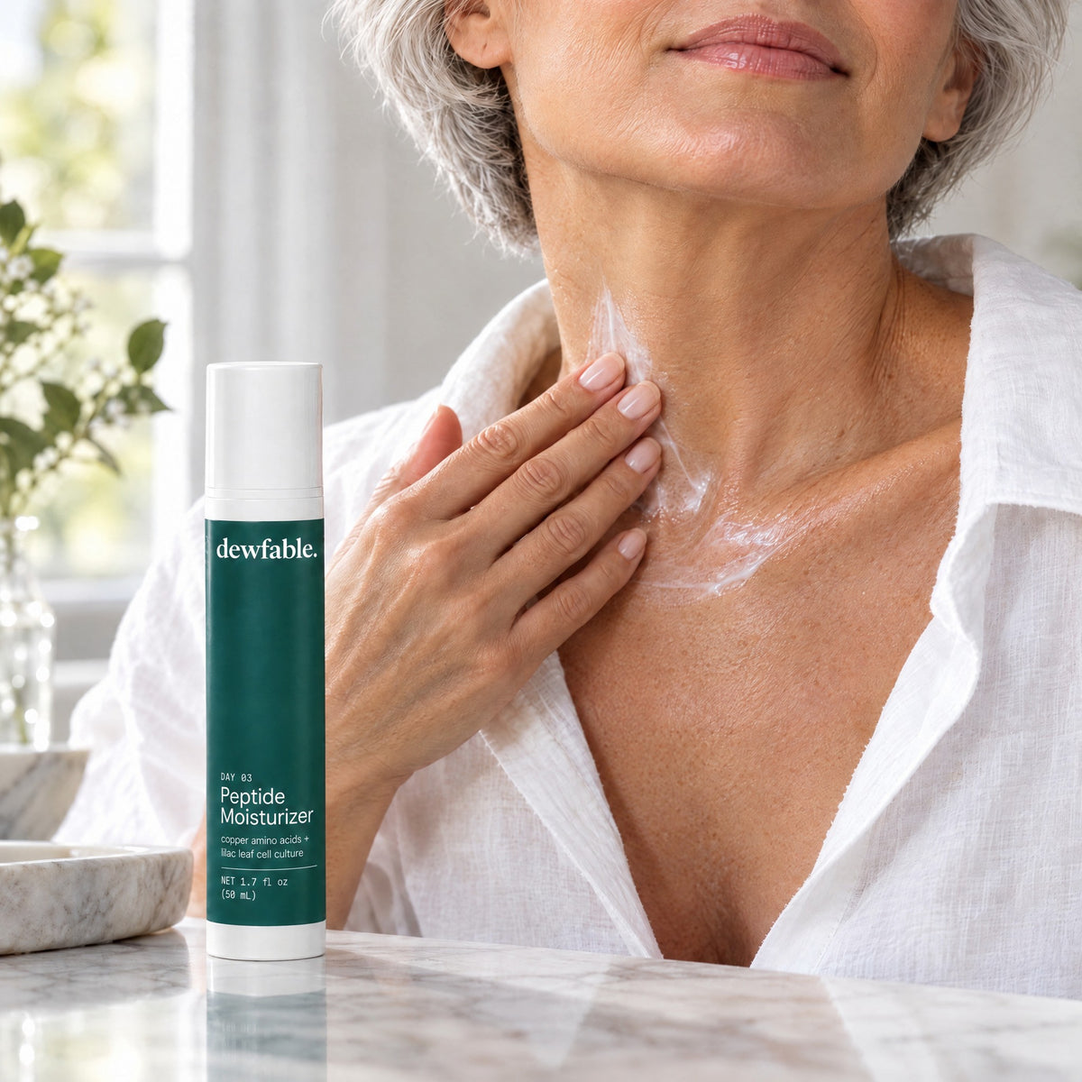 A woman in her fifties smoothing dewfable. Peptide Moisturizer down her neck and chest
